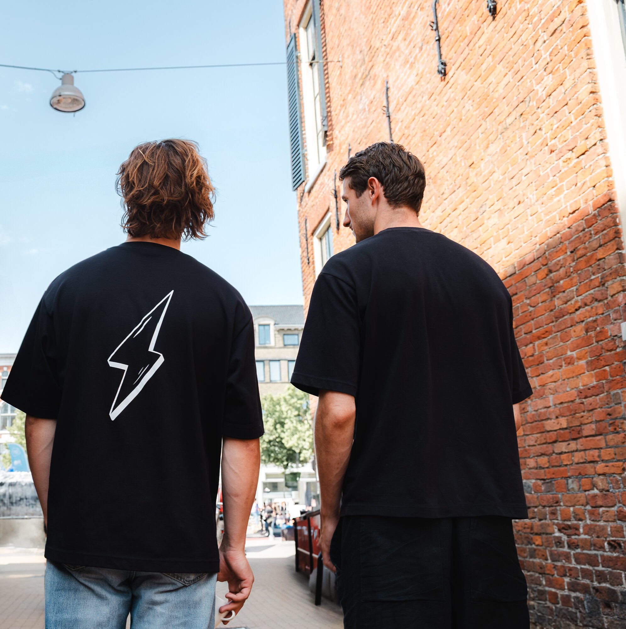 Twee Clubleden op de rug gezien in een Groningse straat, één met de schicht op zijn shirt